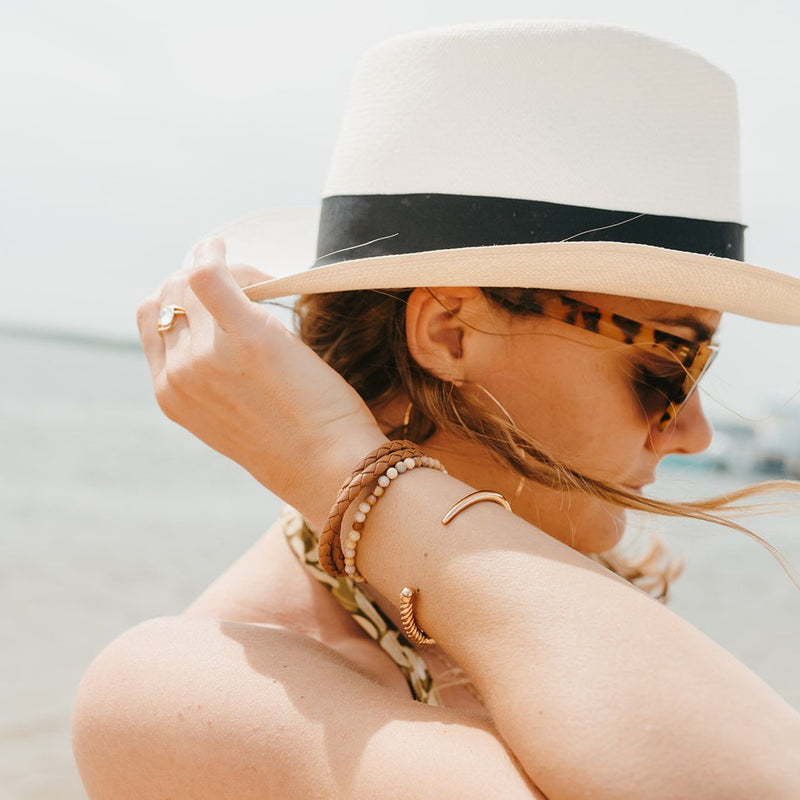 Woman on Plum Island beach wearing Sailormade nautical double wrap leather bracelet with rose gold brummel clasps in baked brown, rayminder uv awareness bracelet in topaz jade, and slim fid cuff in rose gold. Handmade in Boston, MA. 